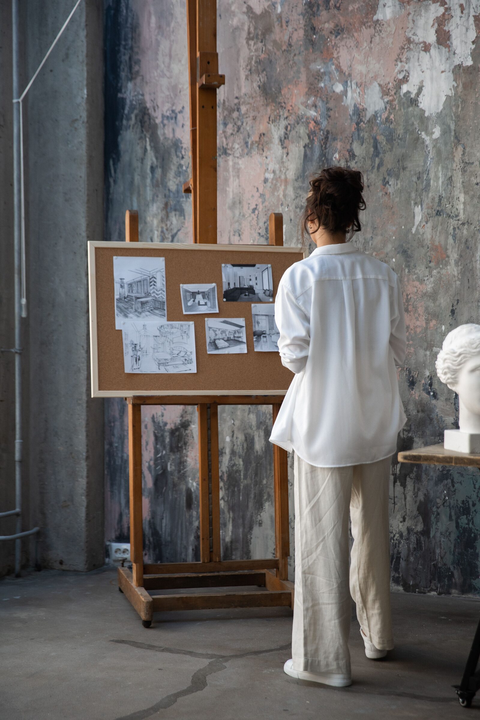 A designer reviews sketches pinned to a corkboard easel in a studio.
