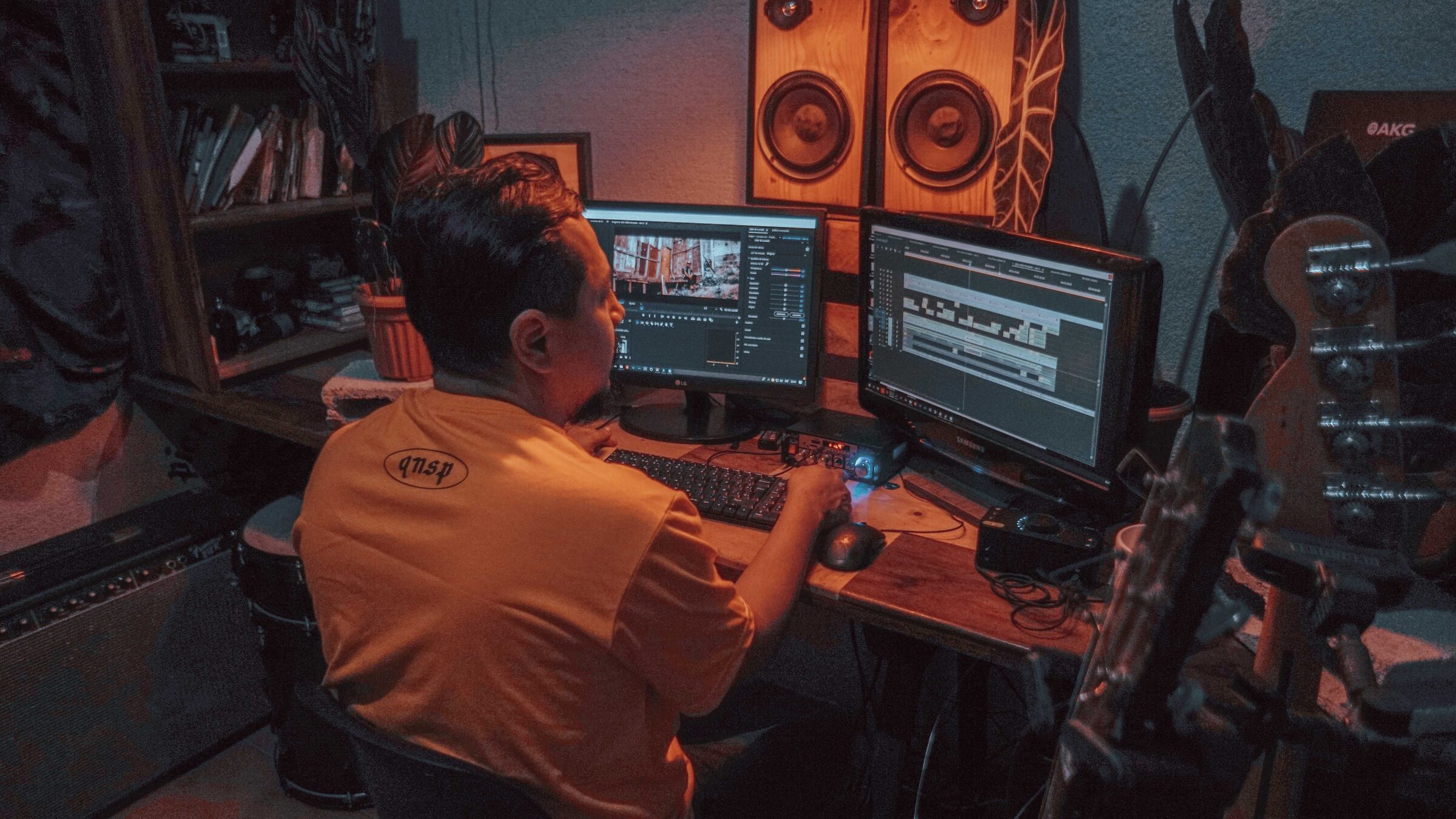 A musician edits footage and audio at a home studio desk surrounded by speakers and instruments.